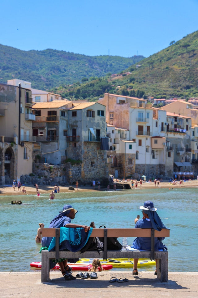 Céfalu Print of two women on a bench by the water, enjoying a moment in picturesque Sicilian town.