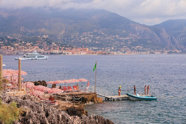 French Beach Print depicting Maybourne La Plage with beach umbrellas and a picturesque view of Roquebrune Cap Martin.