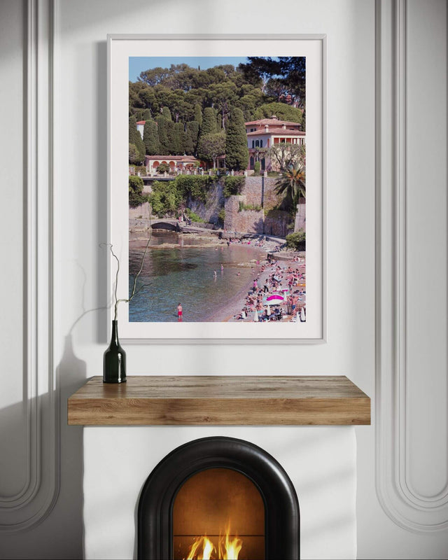 Cap Ferrat Print featuring a beautiful beach scene with vibrant colors on a wall above a wooden mantel.
